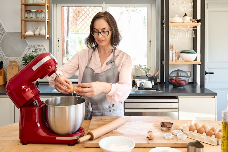 vrouw breekt eieren op keukenmachine om deeg te maken