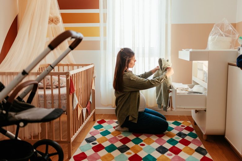 Zwangere vrouw met babykleren in haar hand zittend in de kinderkamer