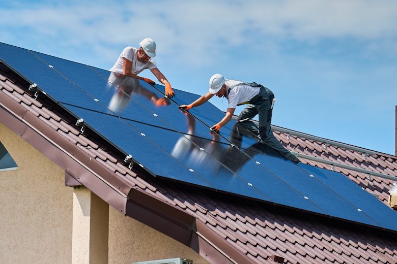 Mannen plaatsen zonnepanelen op het dak van een huis.