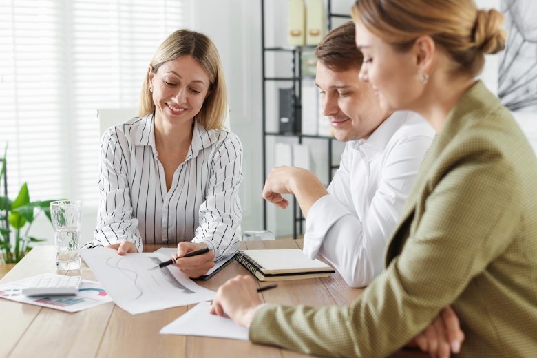 Man en vrouw praten met vrouwelijke adviseur. Op tafel liggen papieren.