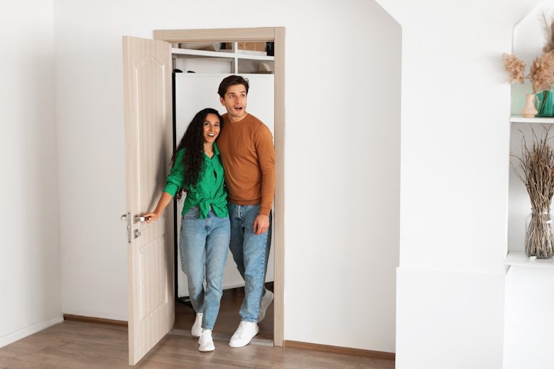 Jong stel, man en vrouw, openen de deur van hun nieuwe huis.