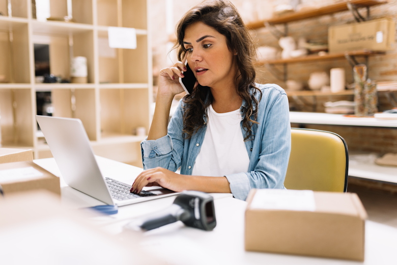 Vrouwelijke ondernemer aan de telefoon terwijl ze een document achter haar laptop zit