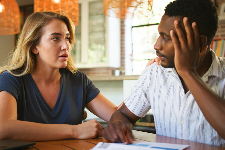 Man en vrouw kijken elkaar bezorgd aan, terwijl ze thuis aan tafel zitten