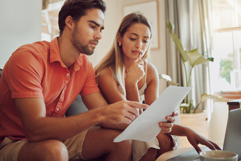 Jongeman en jonge vrouw in zomerse kleding kijken naar een document, met een zorgelijke uitdrukking.
