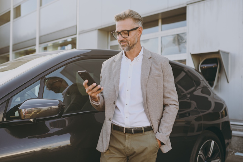 elektrische leaseauto aan de oplader met chauffeur die de laadapp checkt op zijn smartphone